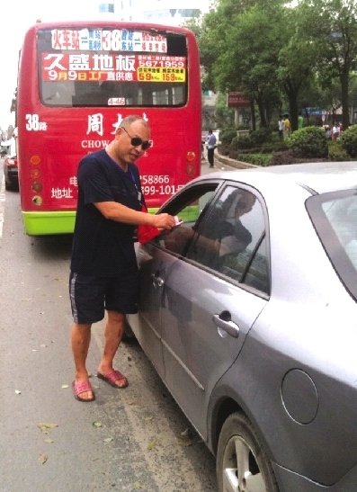 8月17日，邵陽(yáng)市西湖路與寶慶路交接處，穿拖鞋戴墨鏡的市容監(jiān)督員在對(duì)占?jí)喊唏R線停放的車輛罰款。圖/記者龍?jiān)? hspace=